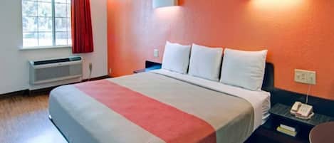 Une chambre d’hôtel avec un lit, une table de chevet avec un téléphone, une fenêtre avec des rideaux et une lampe fixée au mur.