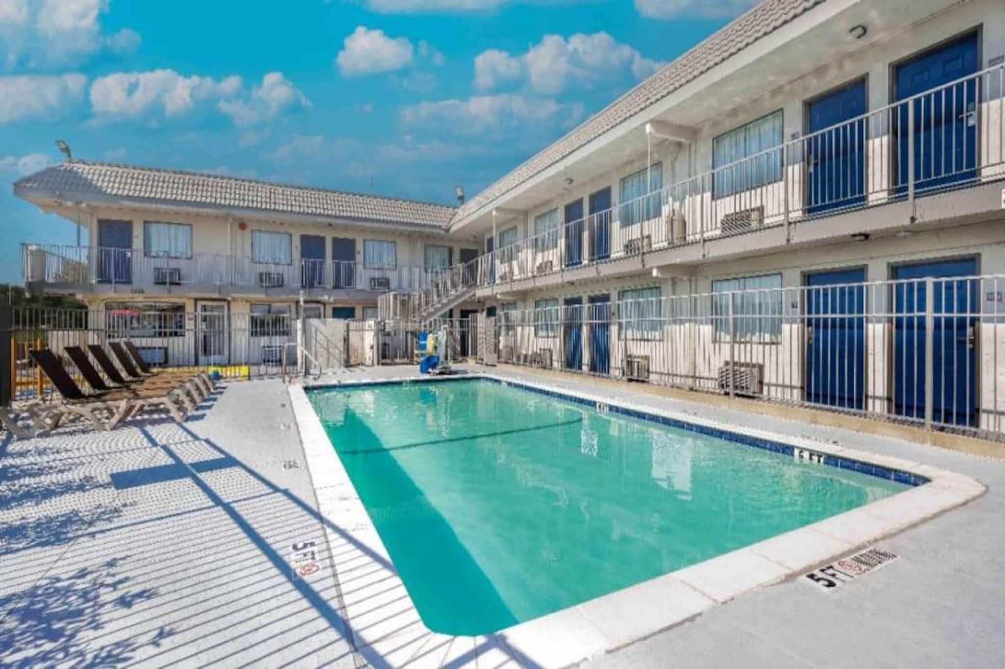 A hotel with a swimming pool, multiple balconies, and a clear sky.
