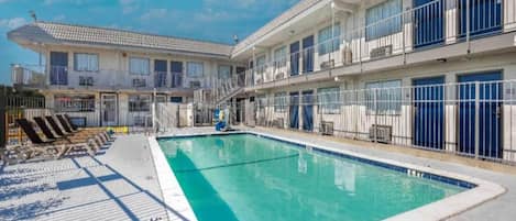 A hotel with a swimming pool, multiple balconies, and a clear sky.