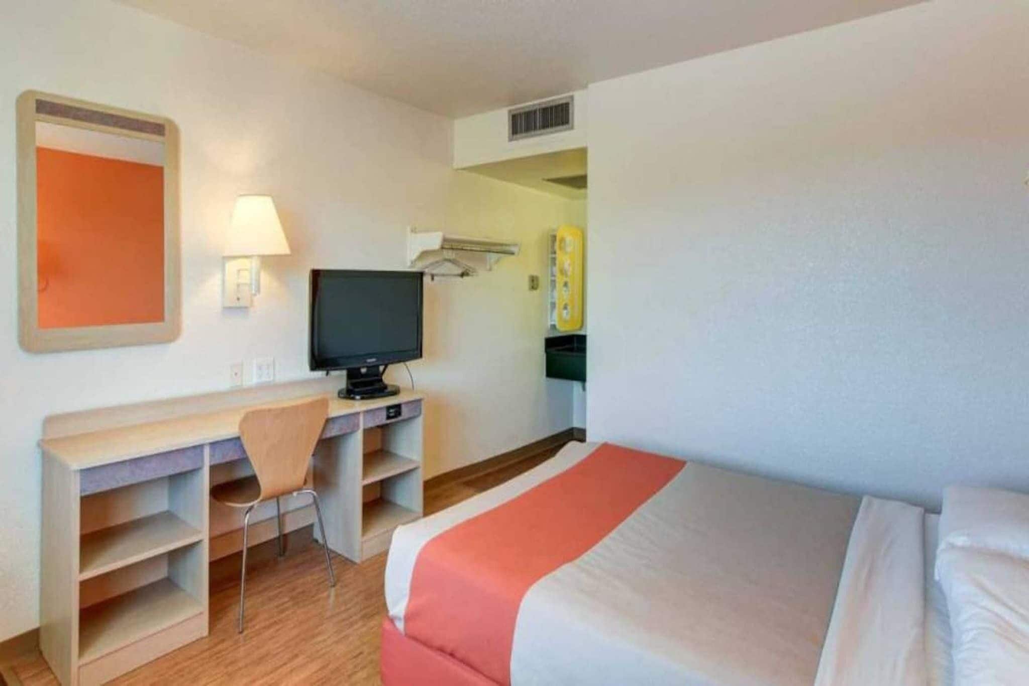 Habitació d'hotel amb un llit, un escriptori, una cadira, una televisió i un aire condicionat fixat a la paret.