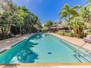 A swimming pool with clear blue water, surrounded by lush greenery and modern buildings. - Bali Resort | Ocean Air Retreat (Kingscliff)