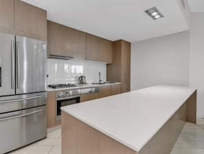 Een moderne keuken met roestvrijstalen apparatuur, houten kastjes en een wit aanrecht.