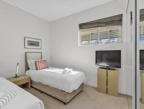 Quarto de hotel moderno com cama, televisão, mesa de cabeceira e janela com persianas.