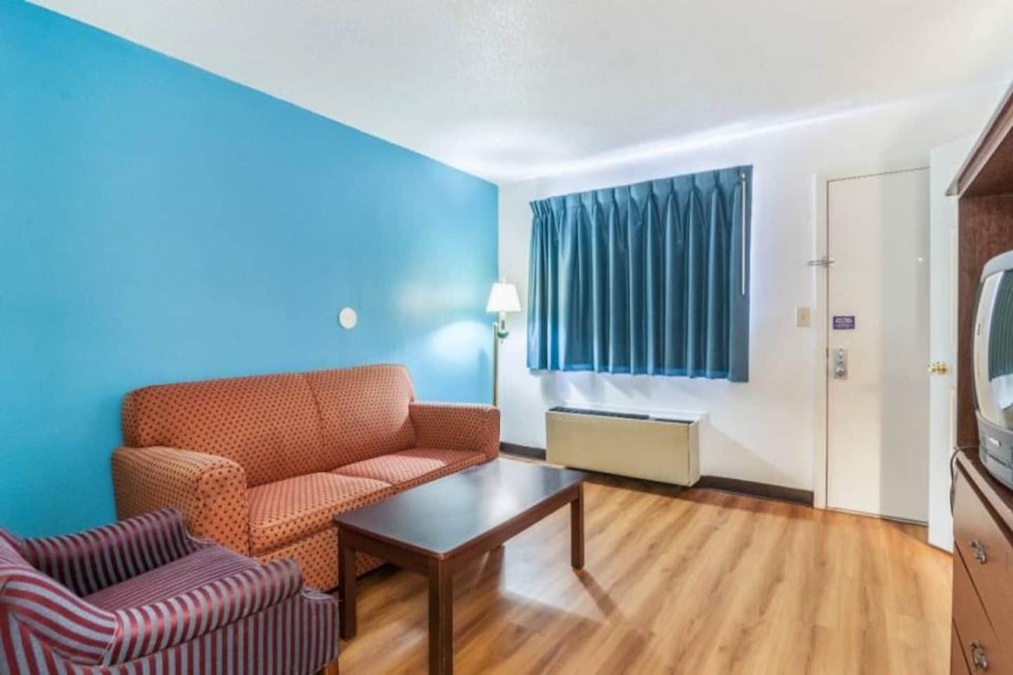 Une pièce comprenant un canapé, un fauteuil à rayures, une table basse en bois, une lampe, une fenêtre avec des rideaux et un téléviseur.