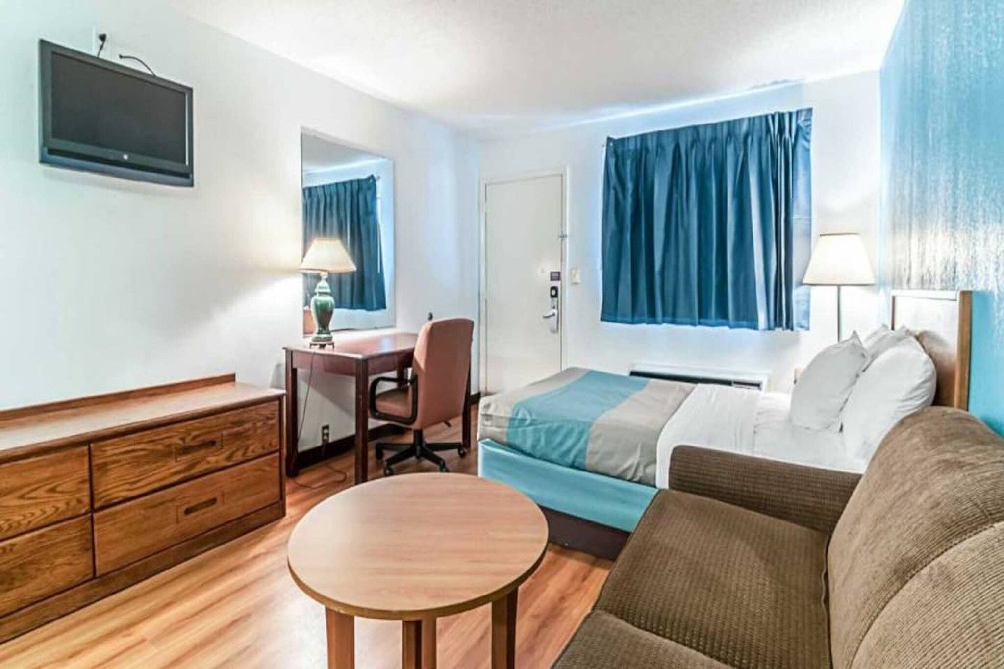 A hotel room with a bed, a desk, a chair, a dresser, and a television.