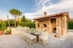 An outdoor patio with a stone-built barbecue area, wicker furniture, and a table set for dining. - Experience Elegant Serenity at Villa Alemanna (Pontetetto)