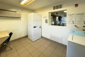 Una sala amb bugaderia que inclou rentadores i assecadores apilades, una finestra i un detector d'incendis fixat a la paret.