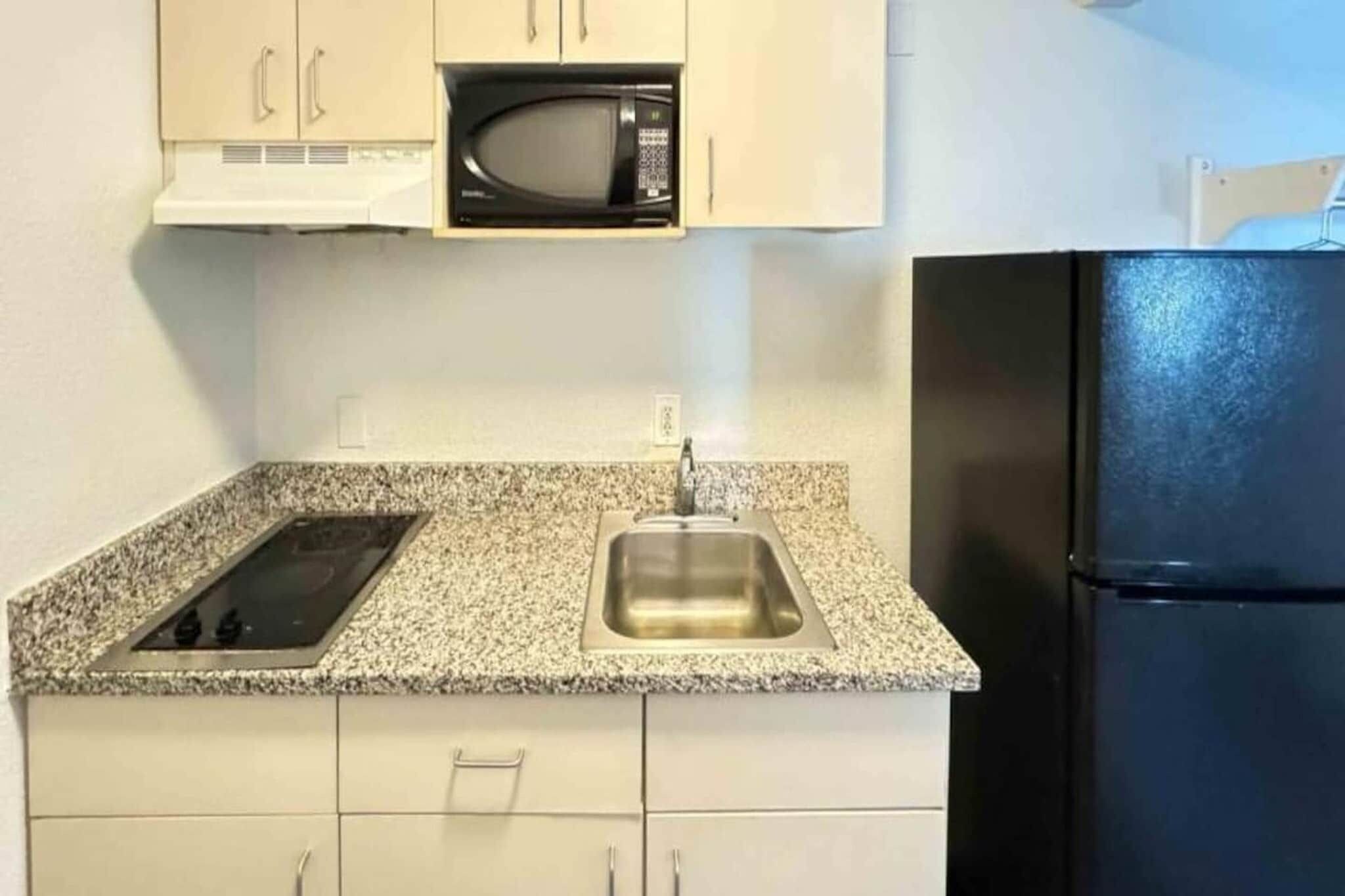 Une cuisine dotée d’un plan de travail en granit, d’un évier en acier inoxydable, d’un four à micro-ondes noir et d’un réfrigérateur noir.