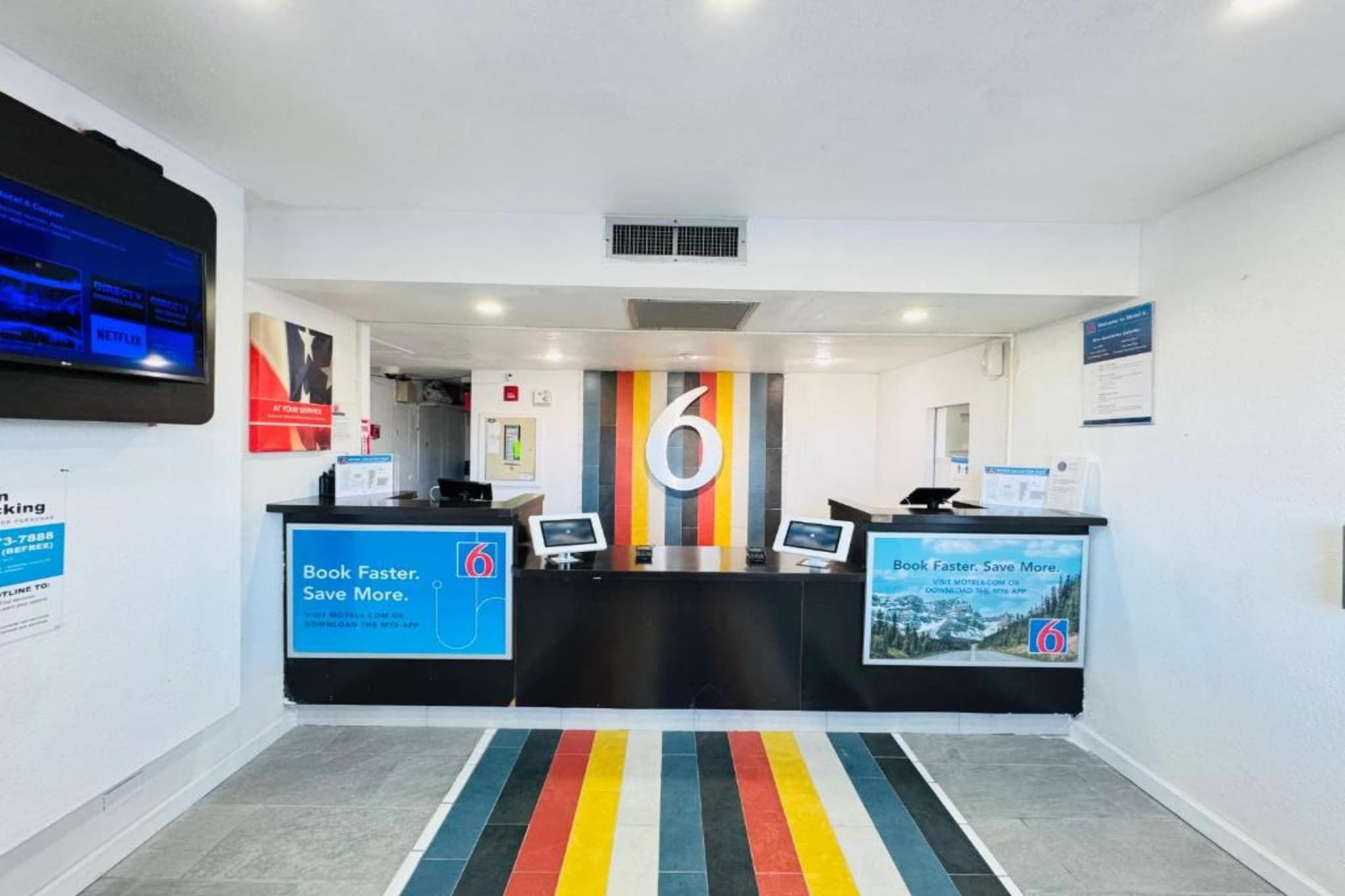 Een hotel receptie met een groot cijfer '6' op de muur, twee balies en een kleurrijk gestreept tapijt.