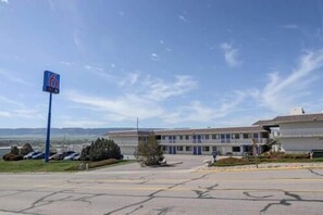 A motel with a large parking lot, a sign indicating the number 6, and a building with multiple windows and a flat roof.