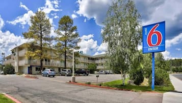 A motel with a parking lot, a building with multiple floors, and a sign indicating the entrance.