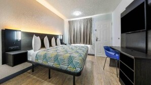 A hotel room with a bed, a desk, a chair, a television, and a door. - 1 Queen Bed | Non-Smoking (Fort Worth TX)