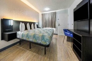 Une chambre d’hôtel avec un lit, un bureau, une chaise, une télévision et une porte.