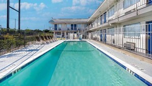A swimming pool with a clear blue water, surrounded by a fence, and a building with multiple balconies in the background. - 1 Queen Bed | Non-Smoking (Fort Worth TX)