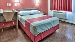 Une chambre d’hôtel avec un lit, un bureau, une chaise, un radiateur et une fenêtre avec des rideaux.