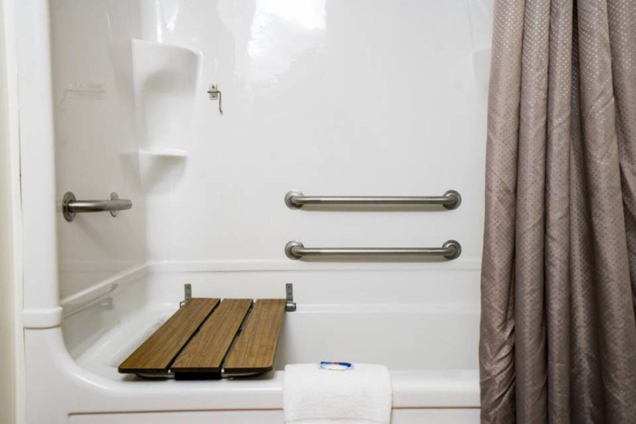 A bathroom with a shower, grab bars, and a wooden bench.