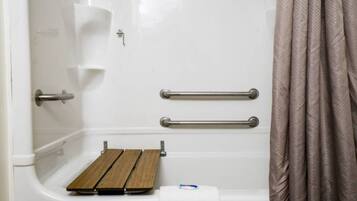 A bathroom with a shower, grab bars, and a wooden bench.