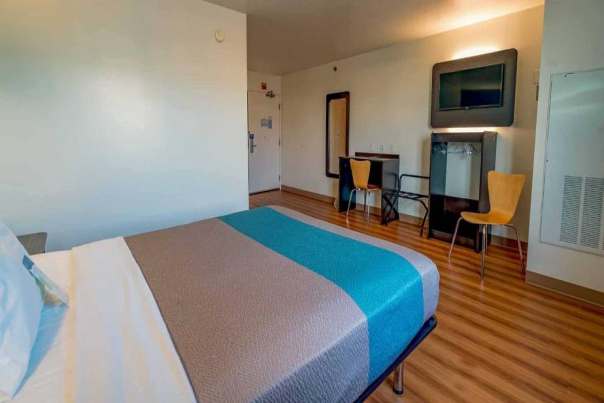 A hotel room with a bed, a desk, a chair, and a television.