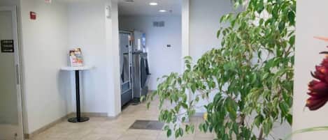 Un couloir avec un sol carrelé, une petite table sur laquelle est posée une pancarte, un réfrigérateur et une plante.