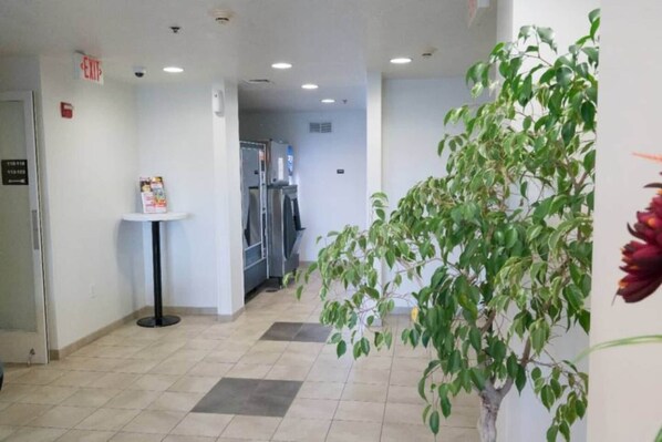 Un passadís amb sòl de rajola, una taula petita amb un cartell, un frigorífic i una planta.