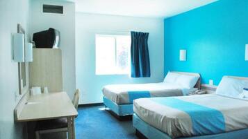 Une chambre d’hôtel avec deux lits, un bureau, une chaise, une fenêtre avec des rideaux et un mur bleu.