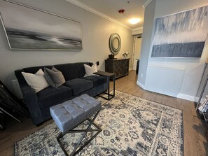 A living room with a dark-colored sofa, a matching ottoman, a coffee table, a patterned rug, and a large abstract painting on the wall. - Ski In and Ski Out Park City Canyons- 3501B (Park City)