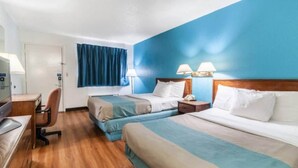 Una camera d'albergo con due letti, una scrivania, una sedia e una finestra con tende.