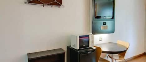 Une pièce de taille modeste, comprenant une petite table et deux chaises, un four à micro-ondes, un meuble noir et un téléviseur fixé au mur.