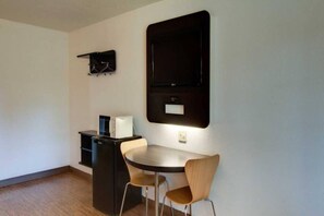 Habitació petita i moderna amb una taula rodona, dues cadires, un moble negre i un televisor penjat.