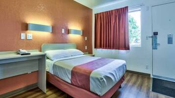Una habitación de hotel con cama, mesita de noche y ventana con cortinas.