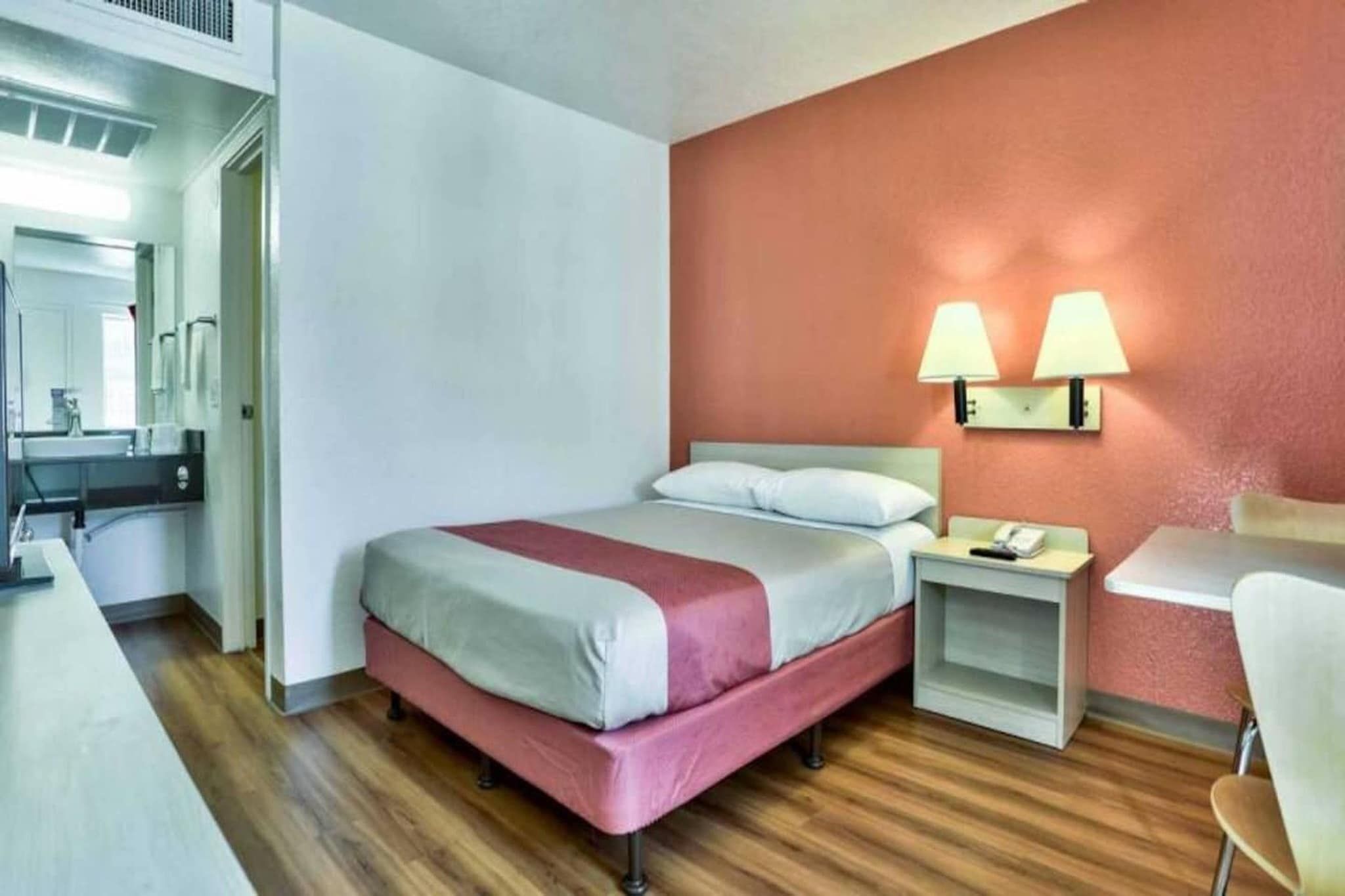 A hotel room with a bed, bedside table, lamp, and a desk with a chair.