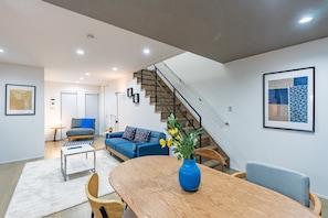 A modern living room with a staircase, a dining area with a wooden table, and a blue sofa. - Nikyo Sumimaru Hikari Private Villa (Osaka)