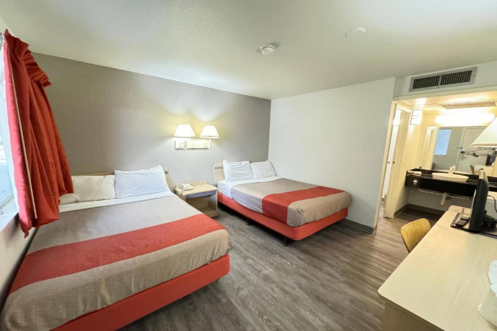 Habitación de hotel con dos camas, un escritorio, una silla, una lámpara y un baño con espejo.