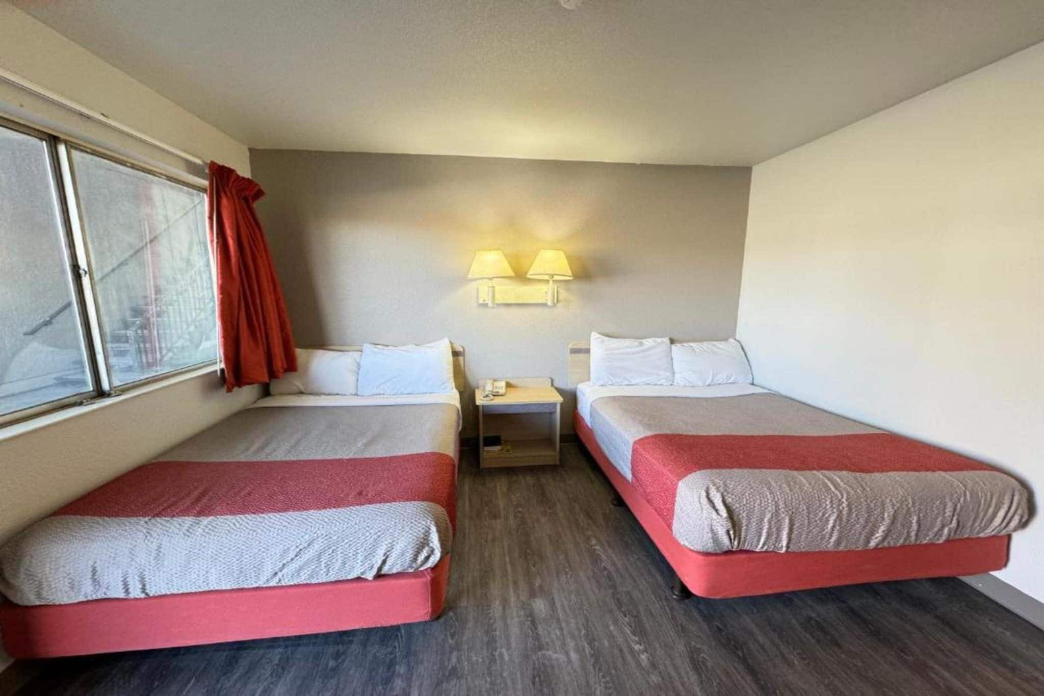 Una camera d'albergo con due letti, un comodino e una finestra con tende.
