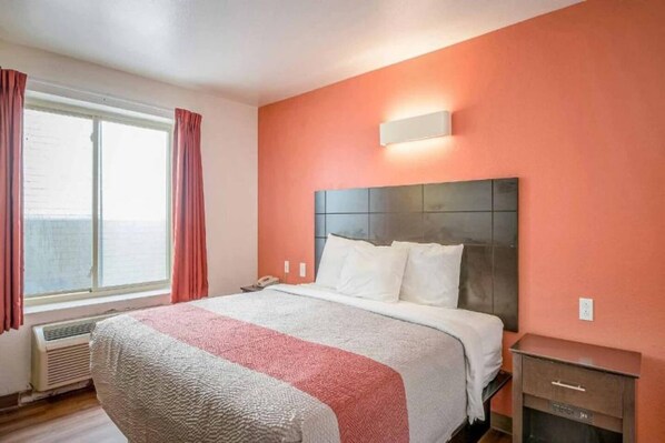 Ein Hotelzimmer mit einem Bett, einem Nachttisch, einer Wandlampe und einem Fenster mit Vorhängen.