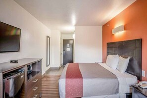 A hotel room with a bed, bedside table, and a TV on the wall. - 1 King Bed | Non-Smoking, Micfridge (Peoria IL)