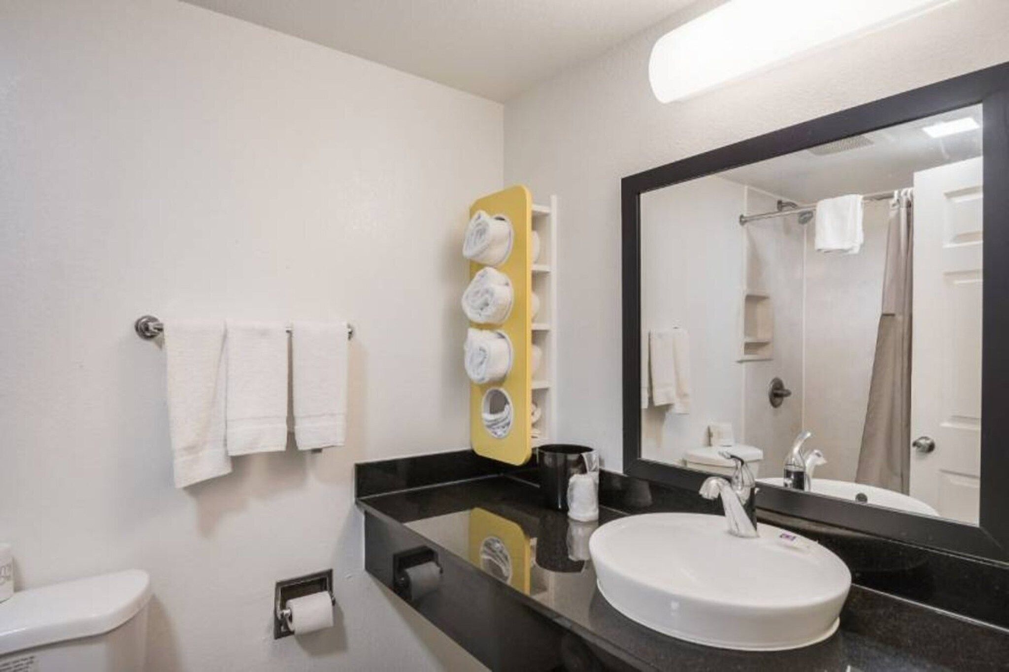A hotel bathroom with a white sink, a large mirror, and a towel rack with multiple towels.