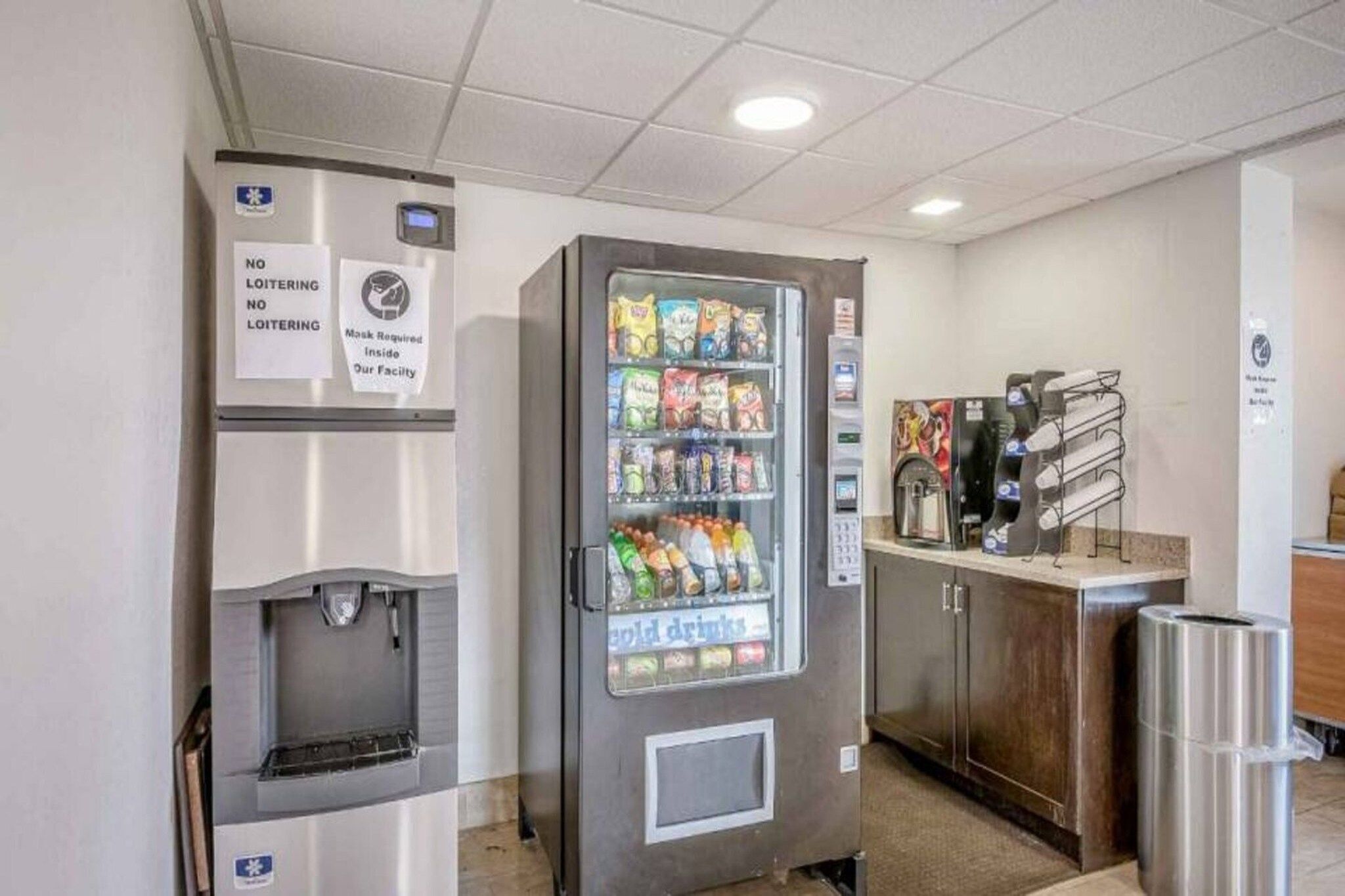 Màquina expenedora amb aperitius i begudes fredes, un dispensador d'aigua i una cafetera en un entorn comercial.