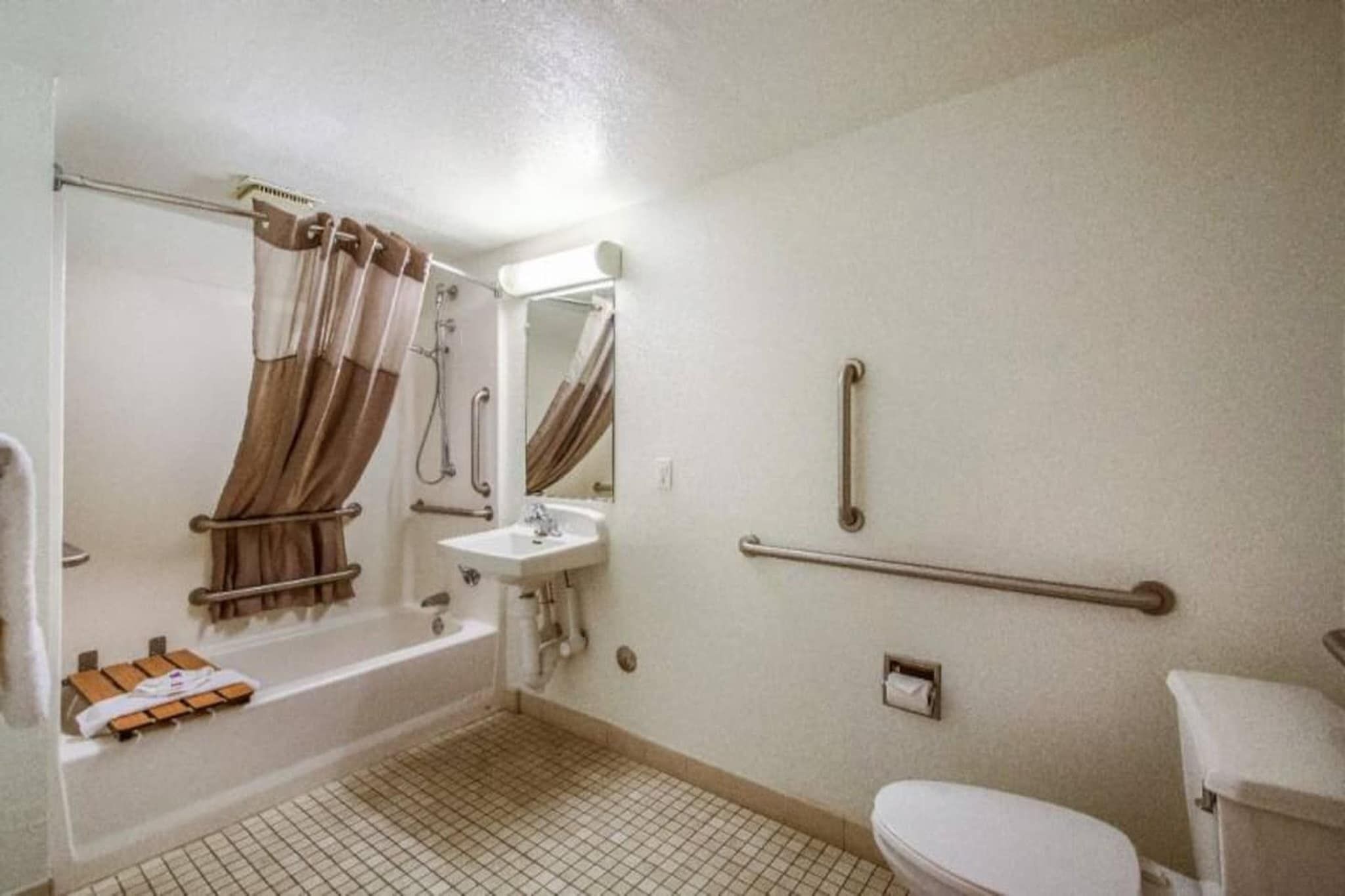 Un baño estándar con bañera, lavamanos, inodoro y barras de apoyo.