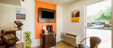 Ein Empfangsbereich mit Theke, einem an der Wand befestigten Fernseher, einem Stuhl und einem Fenster mit Blick auf einen Parkplatz.