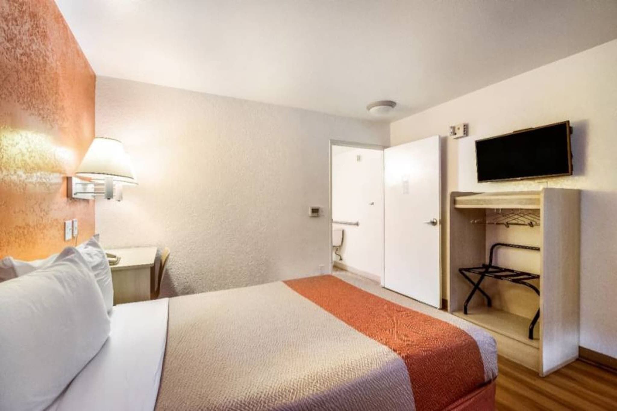 Ein Hotelzimmer mit Bett, Schreibtisch, Wandfernseher und Kleiderschrank.