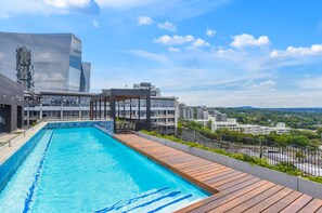 Piscina no terraço com vista para edifícios ao redor e céu limpo.