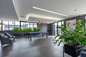 Espaço de escritório moderno com mesa de bilhar, área de estar e janelas amplas.