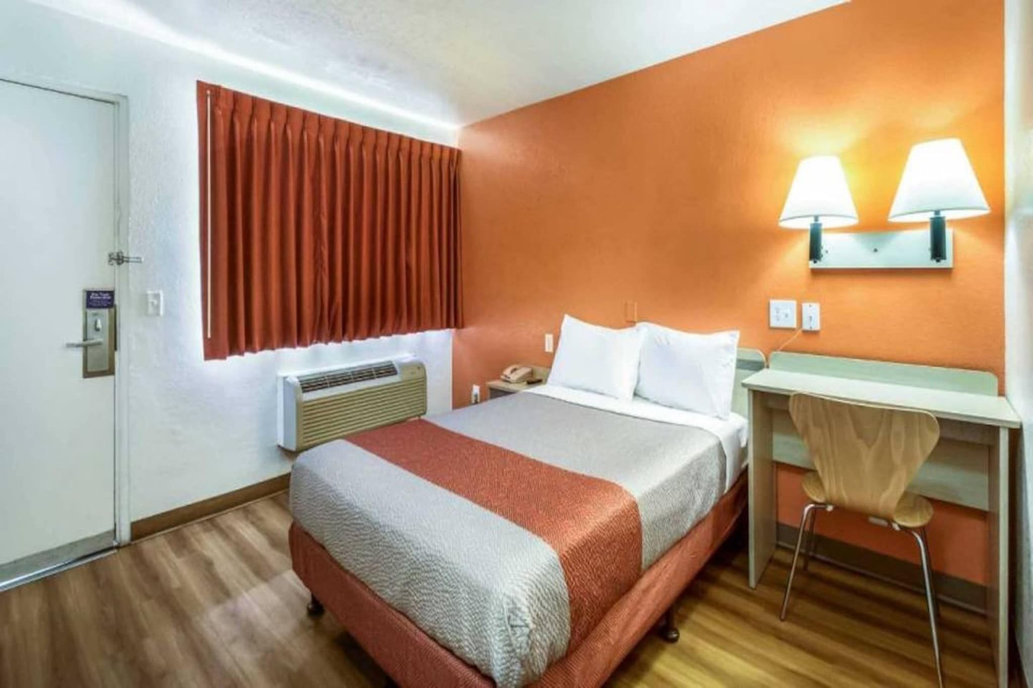 Ein Hotelzimmer mit Bett, Nachttisch, Lampe und Klimaanlage.