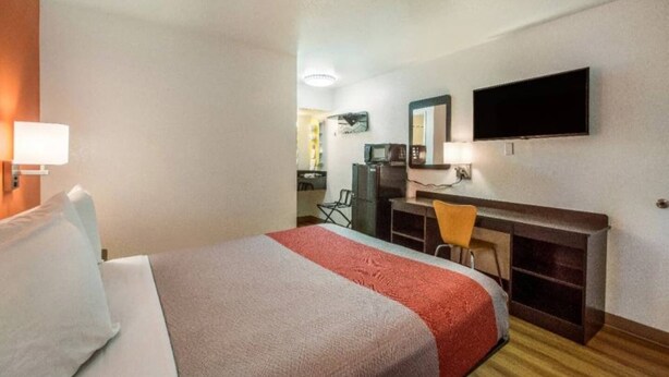 Habitación de hotel con cama, escritorio, silla, televisor y espejo.