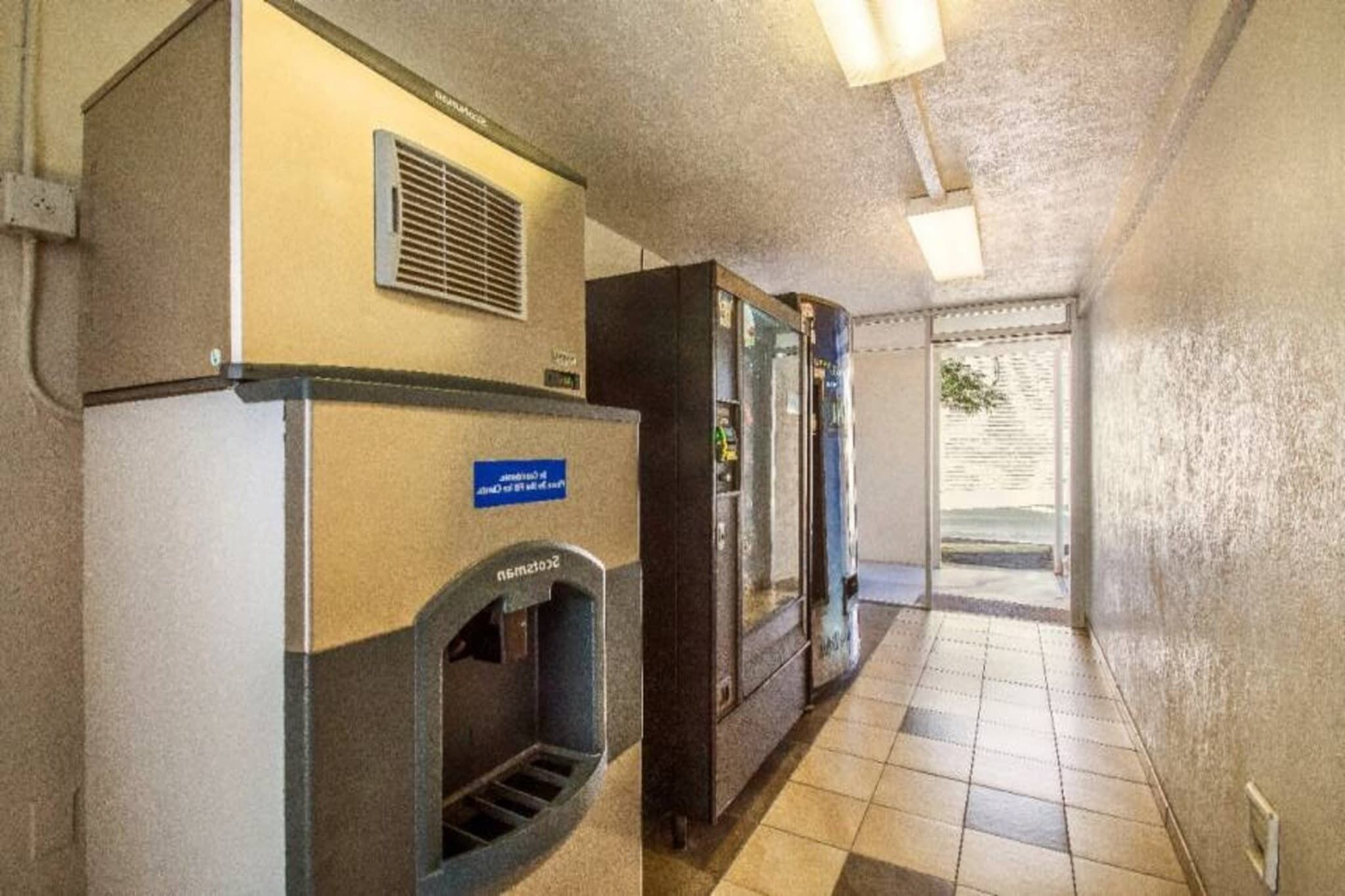 Un pasillo con una máquina expendedora, un refrigerador y una puerta que da a un área exterior.