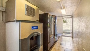 Un pasillo con una máquina expendedora, un refrigerador y una puerta que da a un área exterior.