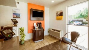 Zona de recepción con mostrador, televisor montado en la pared, una silla y ventana con vista al estacionamiento.