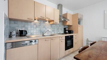 A modern kitchen with light wood cabinets, a stainless steel dishwasher, a built-in oven, and a coffee maker.