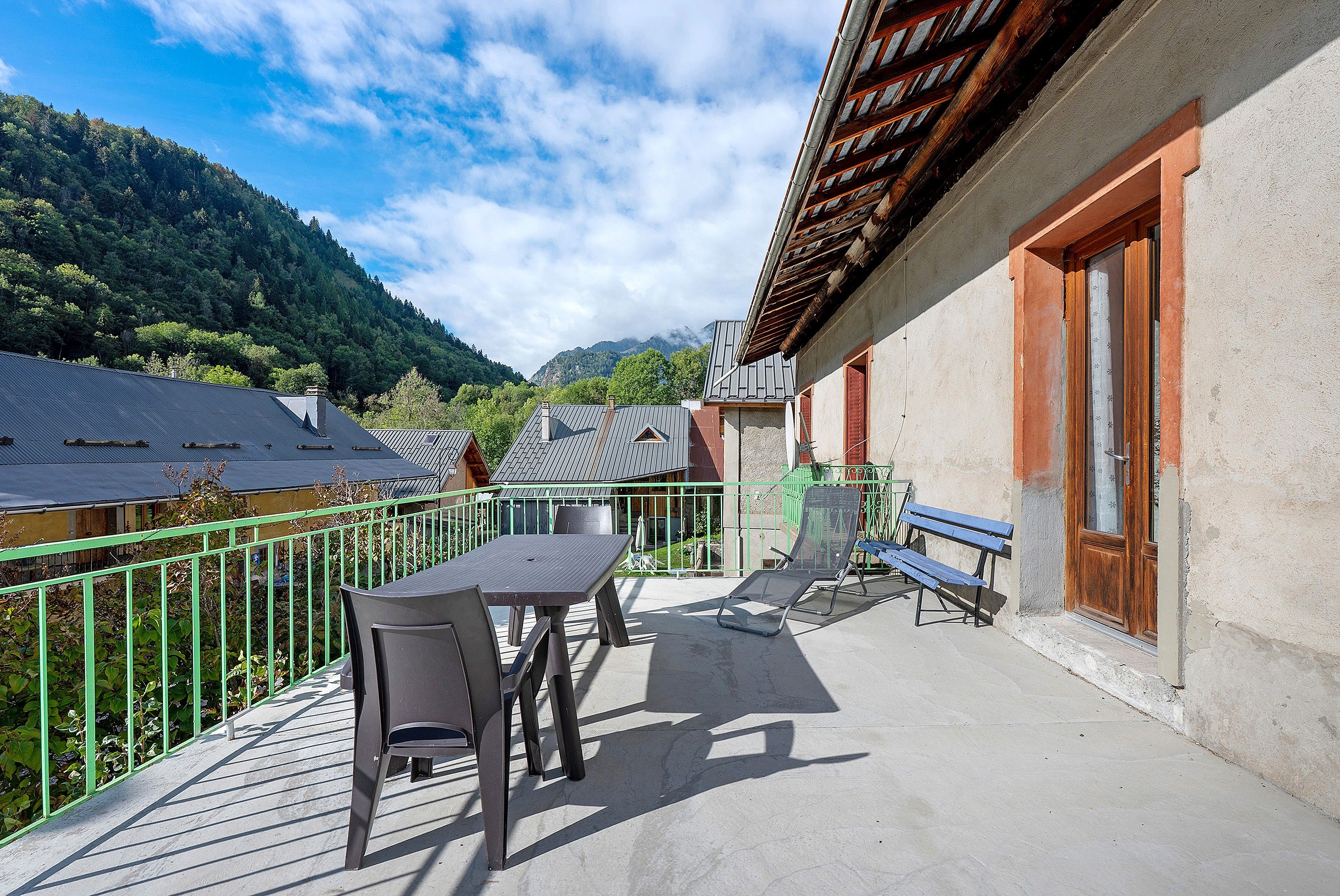 A balcony with a table and chairs, a bench, and a view of a mountain.